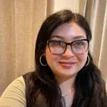 Latina woman in a yellow shirt poses in front of a curtain for a selfie